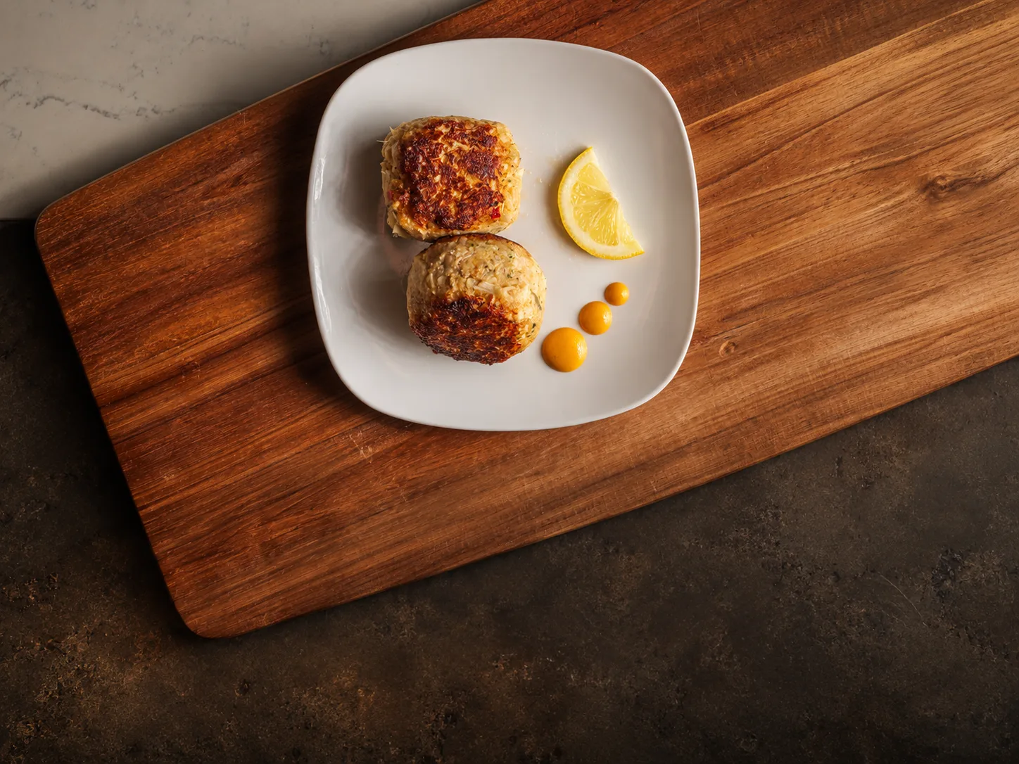 Crab cakes with lemon and a citrus sauce on a wooden board