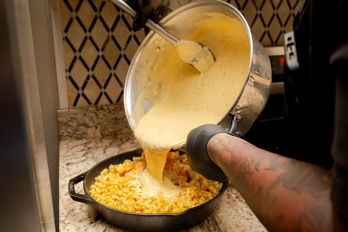 Cheese sauce poured over mac and cheese in a cast-iron skillet